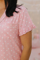 Person wearing a pink polka dot pj set with ruffled sleeves against a blurred background