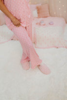 Person wearing pink polka dot pajamas sitting on a white bed with pink polka dot slippers