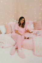 Woman in pink pajamas sitting on a pink couch with a cozy, lit background