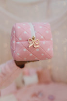 Pink polka dot bag with a gold bow charm held by a hand against a blurred background