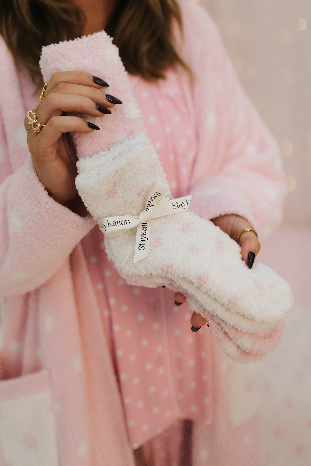 Person holding pink polka scoks wearing a pink robe.