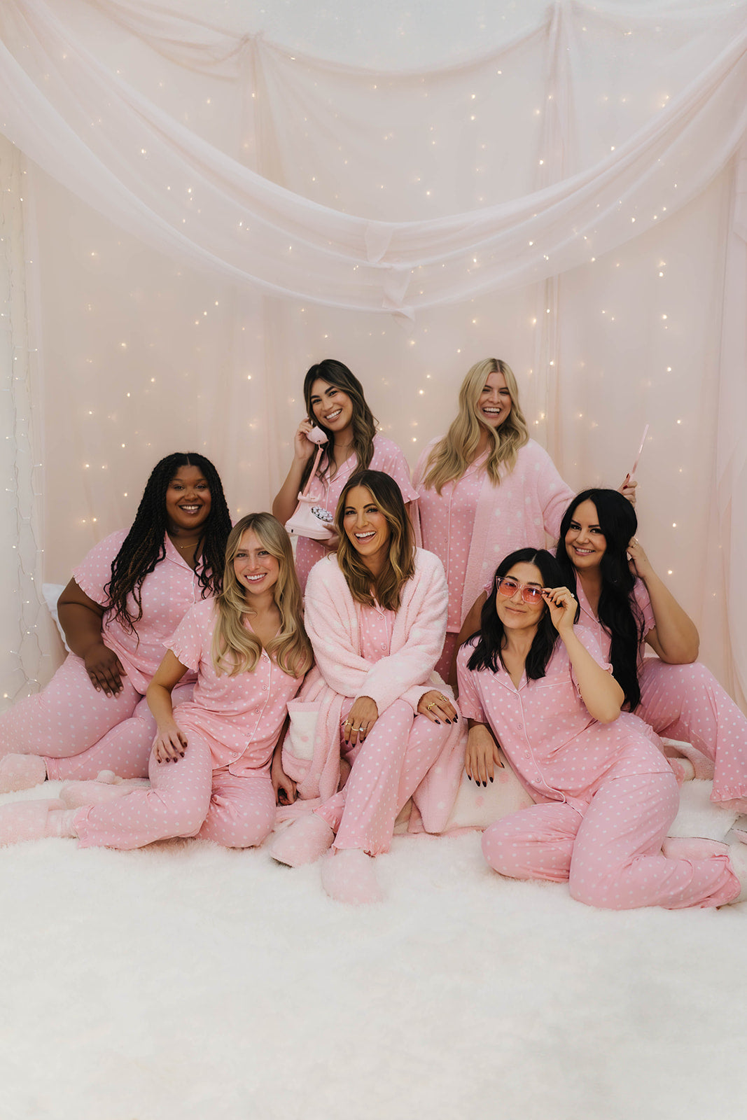Group of women in pink robes posing together against a soft, light background.