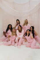 Group of women in pink pjs and robes posing together against a soft, light background.