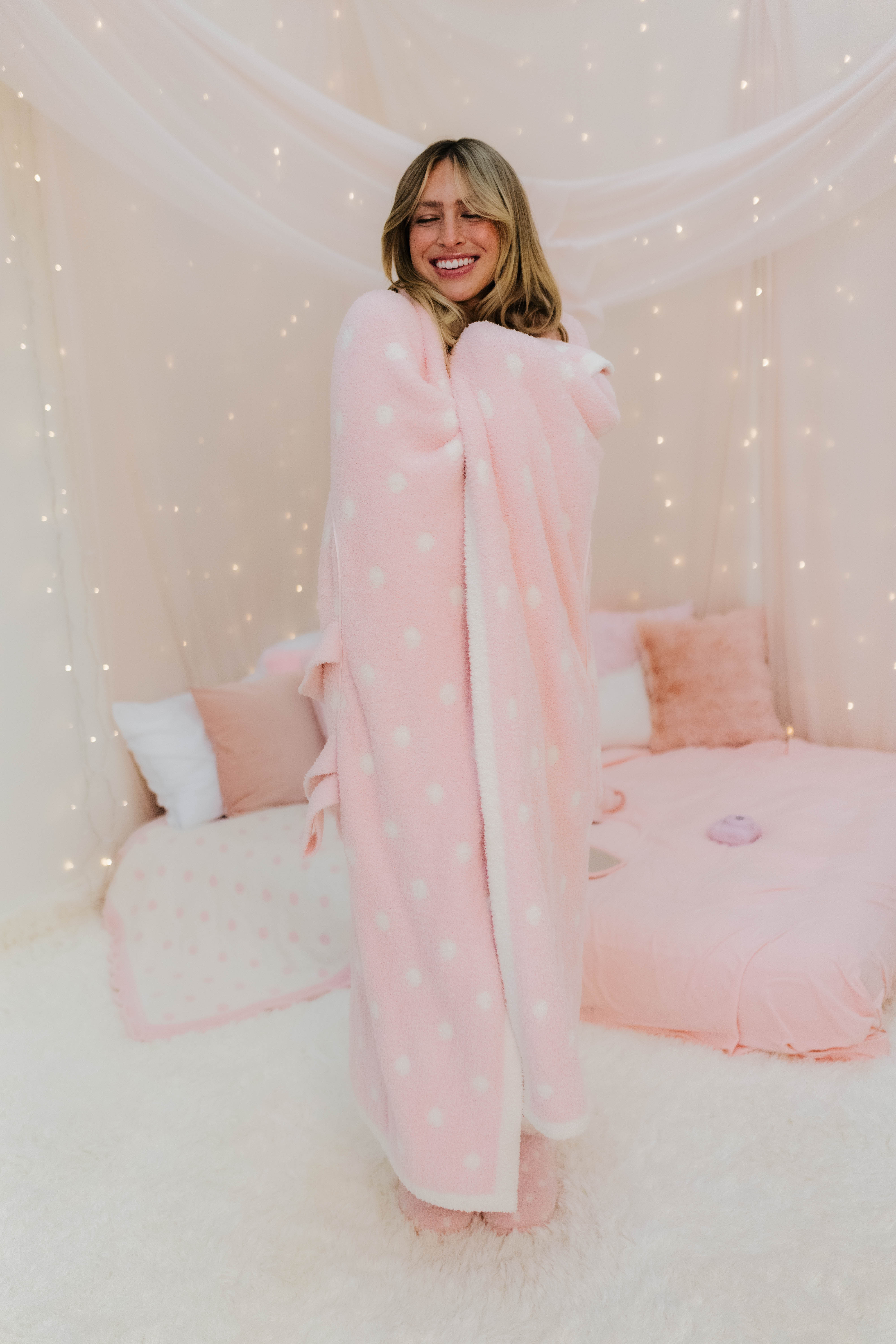 Woman wrapped in a pink polka dot  blanket in a cozy room.