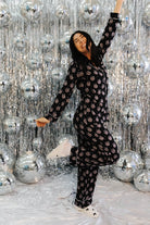 Person in a black patterned outfit posing in front of a silver disco ball curtain.