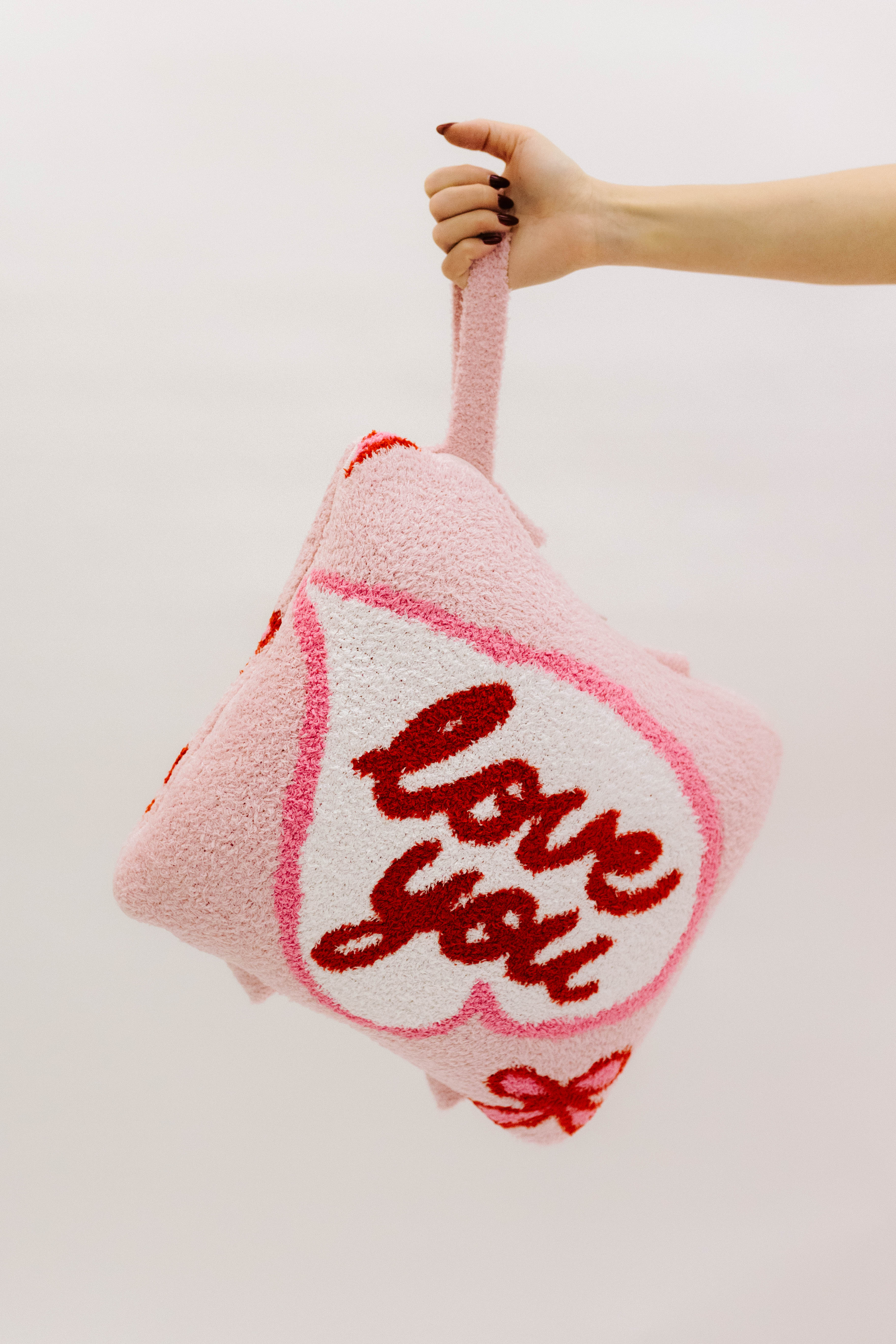 Pink pillow with 'love you' text held by a hand against a light background