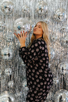 Woman holding a disco ball in front of a sparkling silver curtain