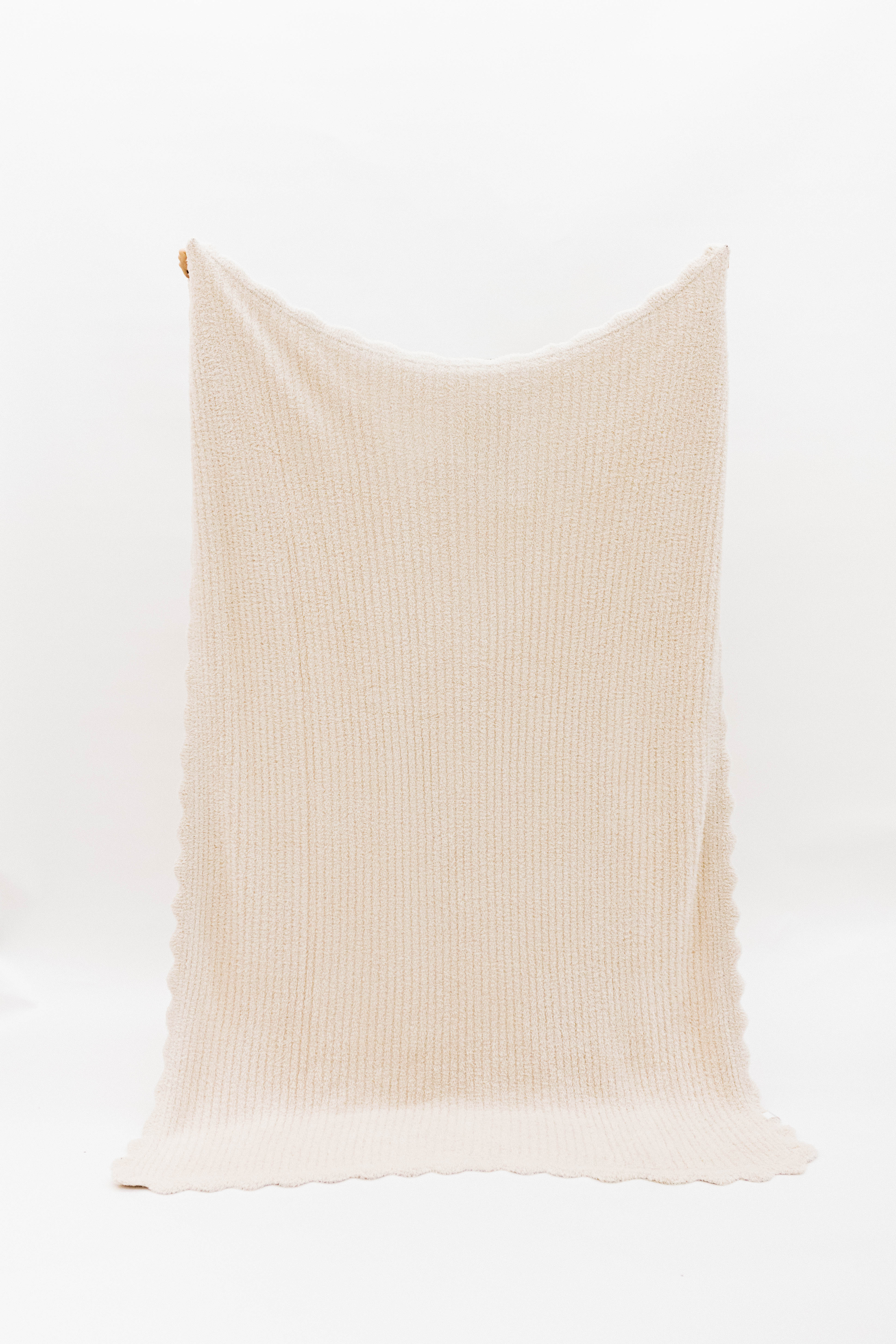 Beige ribbed blanket with scalloped edges on a white background