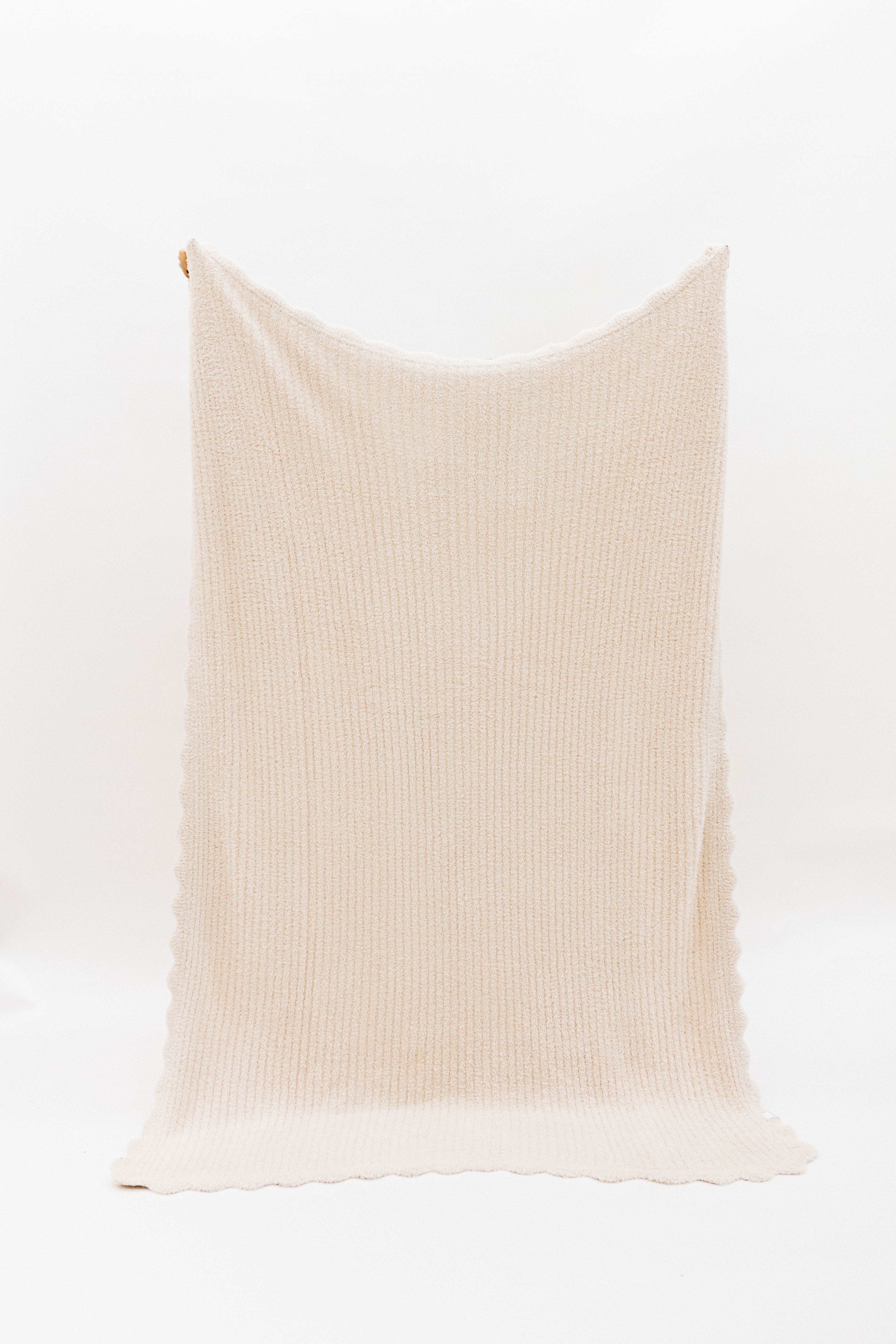 Beige ribbed blanket with scalloped edges on a white background