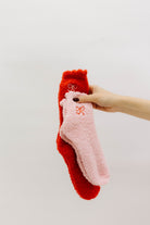 Hand holding two pairs of socks, one red and one pink, against a light background