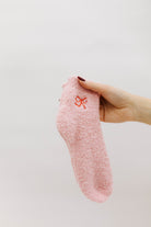 Pink textured sock with a bow print held by a hand against a light background