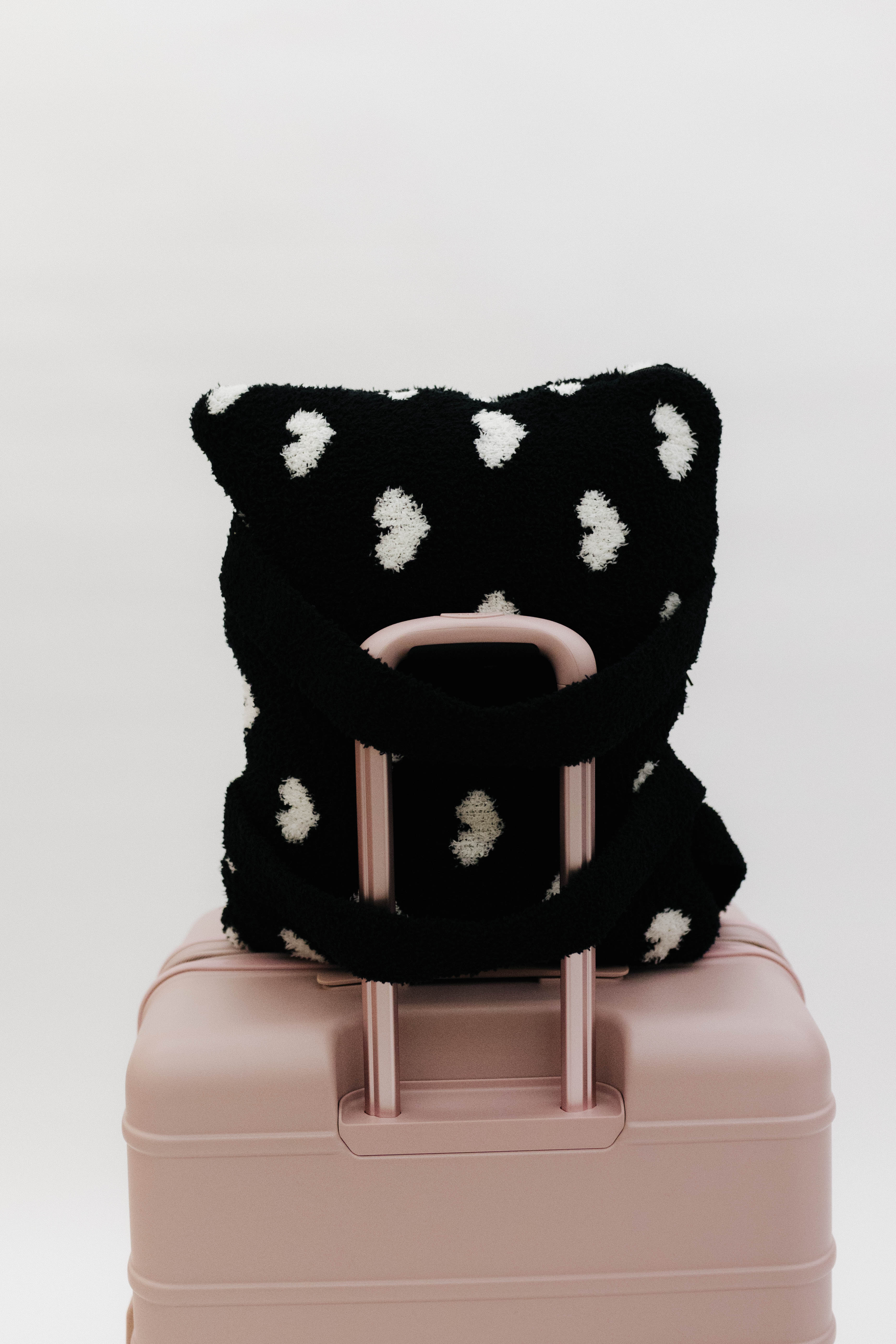 Black and white polka dot quillow on a pink suitcase against a white background