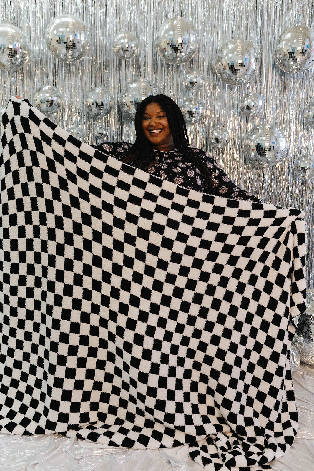 Person holding a large black and white checkered blanket in front of a sparkling silver curtain.