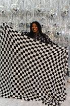Person holding a large black and white checkered blanket in front of a sparkling silver curtain.