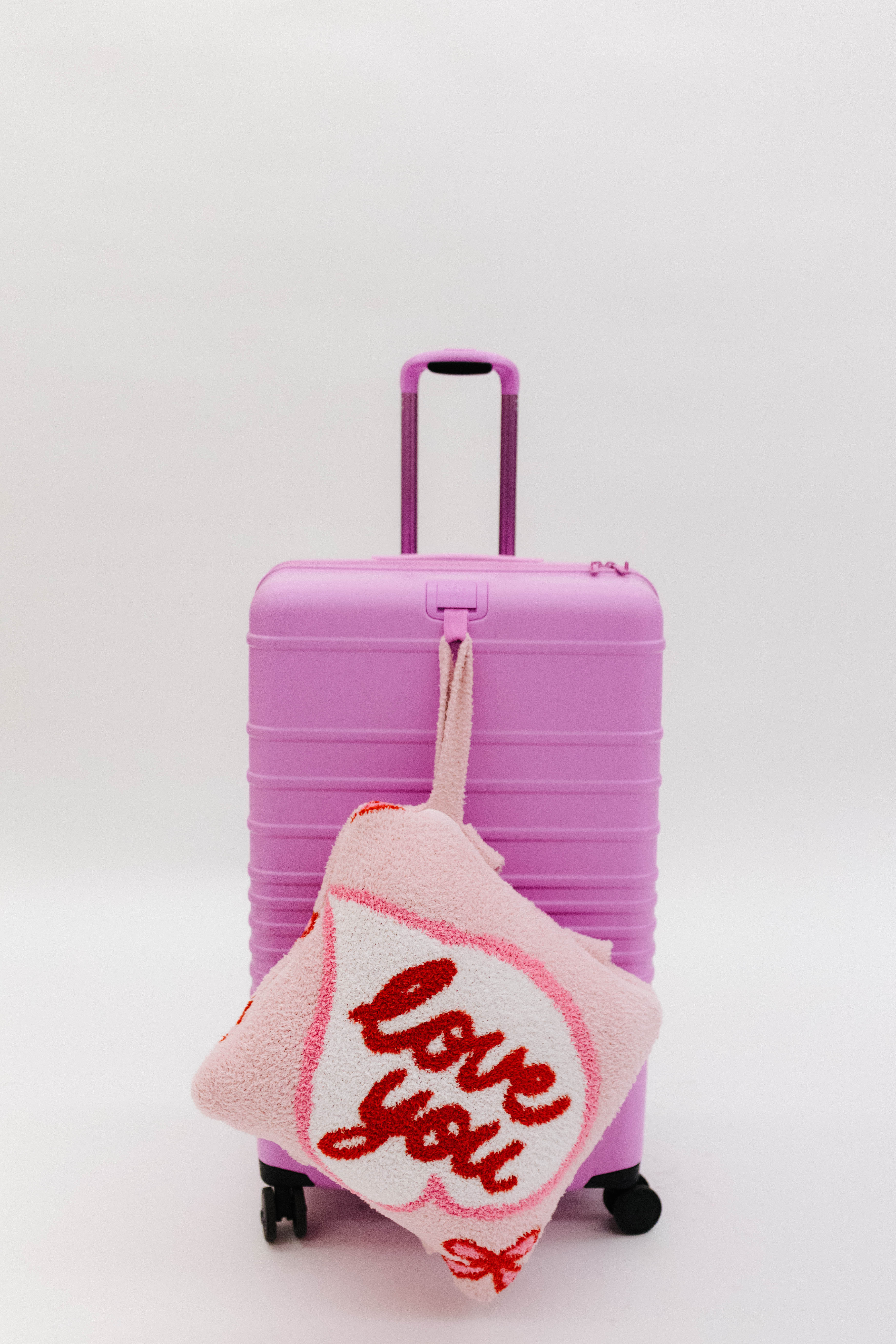 Pink suitcase with a 'love you' quillow attached on a white background