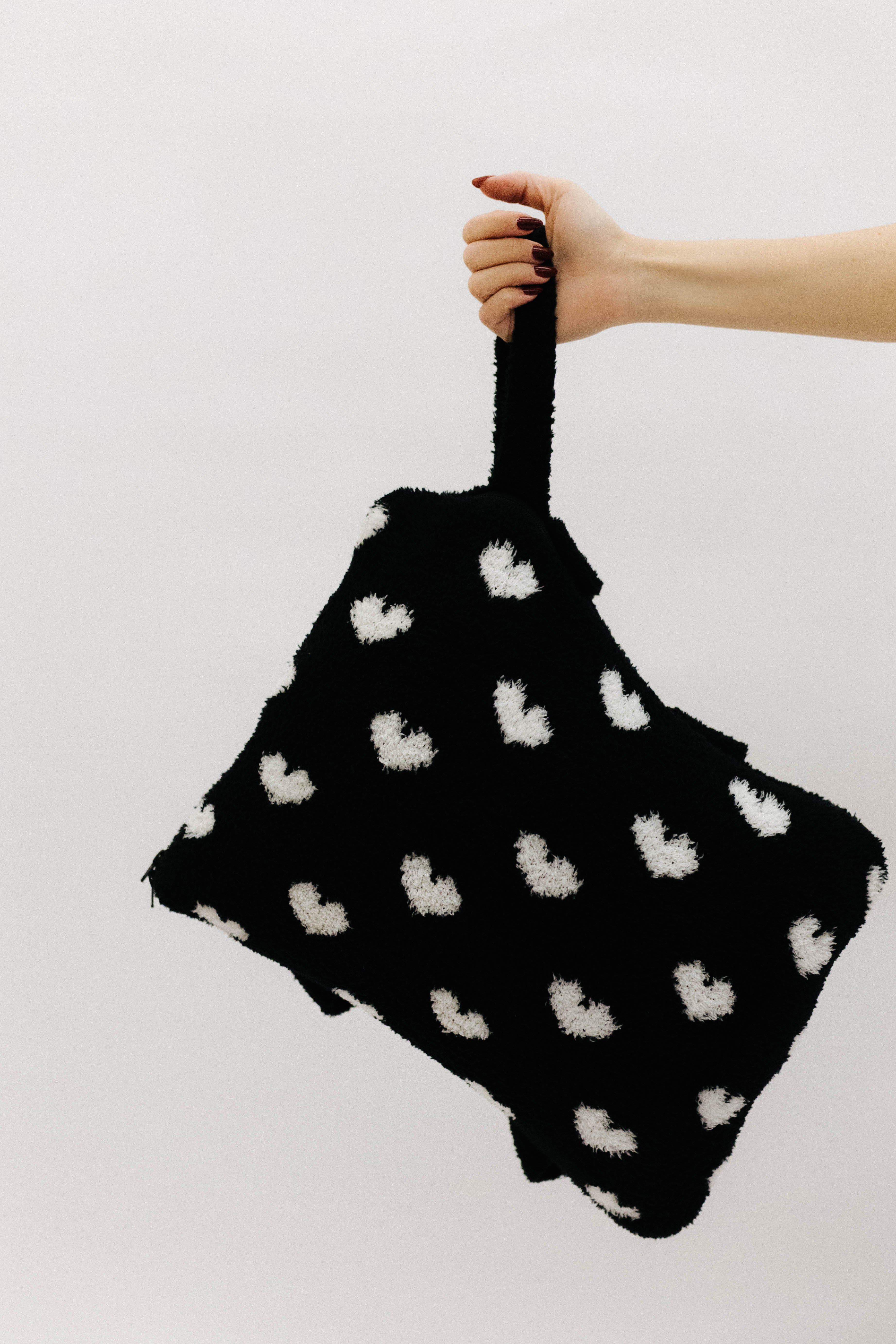 Black bag with white heart patterns held by a hand 