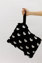 Black bag with white heart patterns held by a hand 