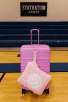 A pink hard-shell suitcase with a volleyball quillow handing off the front of it 