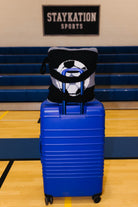 A bright blue hard-shell rolling suitcase stands on an indoor gym floor showing the backside of the quillow.