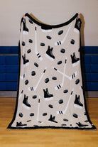 front of hockey blanket being held up showing the black border, skates, sticks, and pucks 