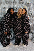 Three women wearing matching black pajamas in front of a silver tinsel background.