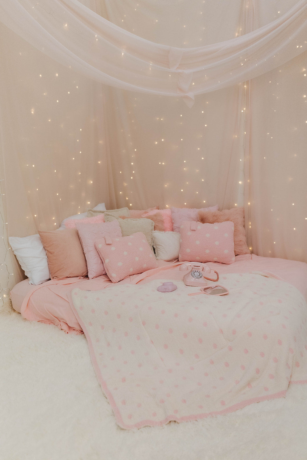 Pink polka dot bedding against a wall with fairy lights