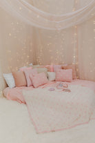 Pink polka dot bedding against a wall with fairy lights
