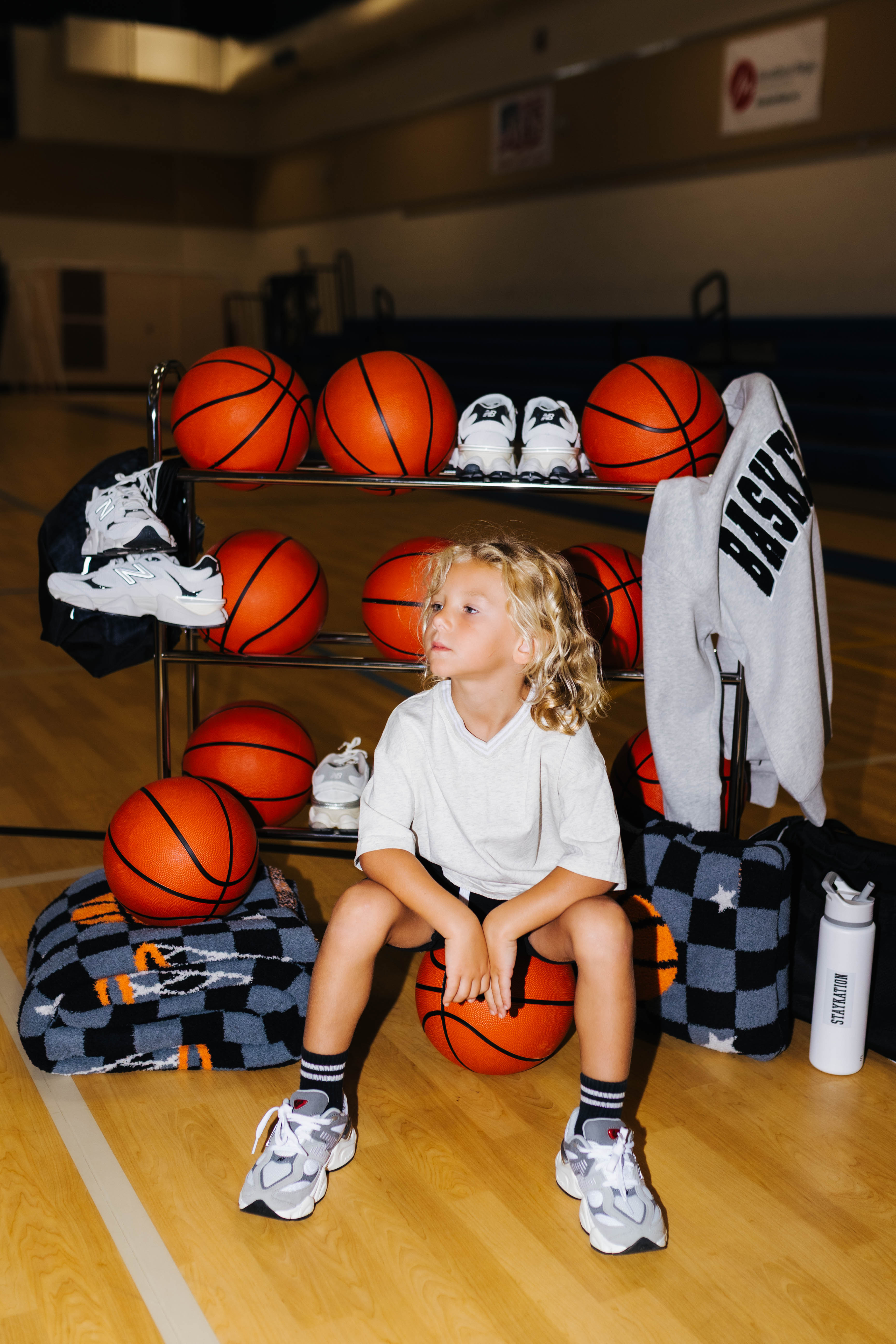 Kamp sitting on a basketball with basketball rack decorated and blankets behind him
