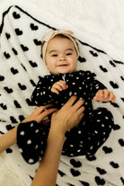 Baby in a black polka dot outfit lying on a white blanket with black heart patterns