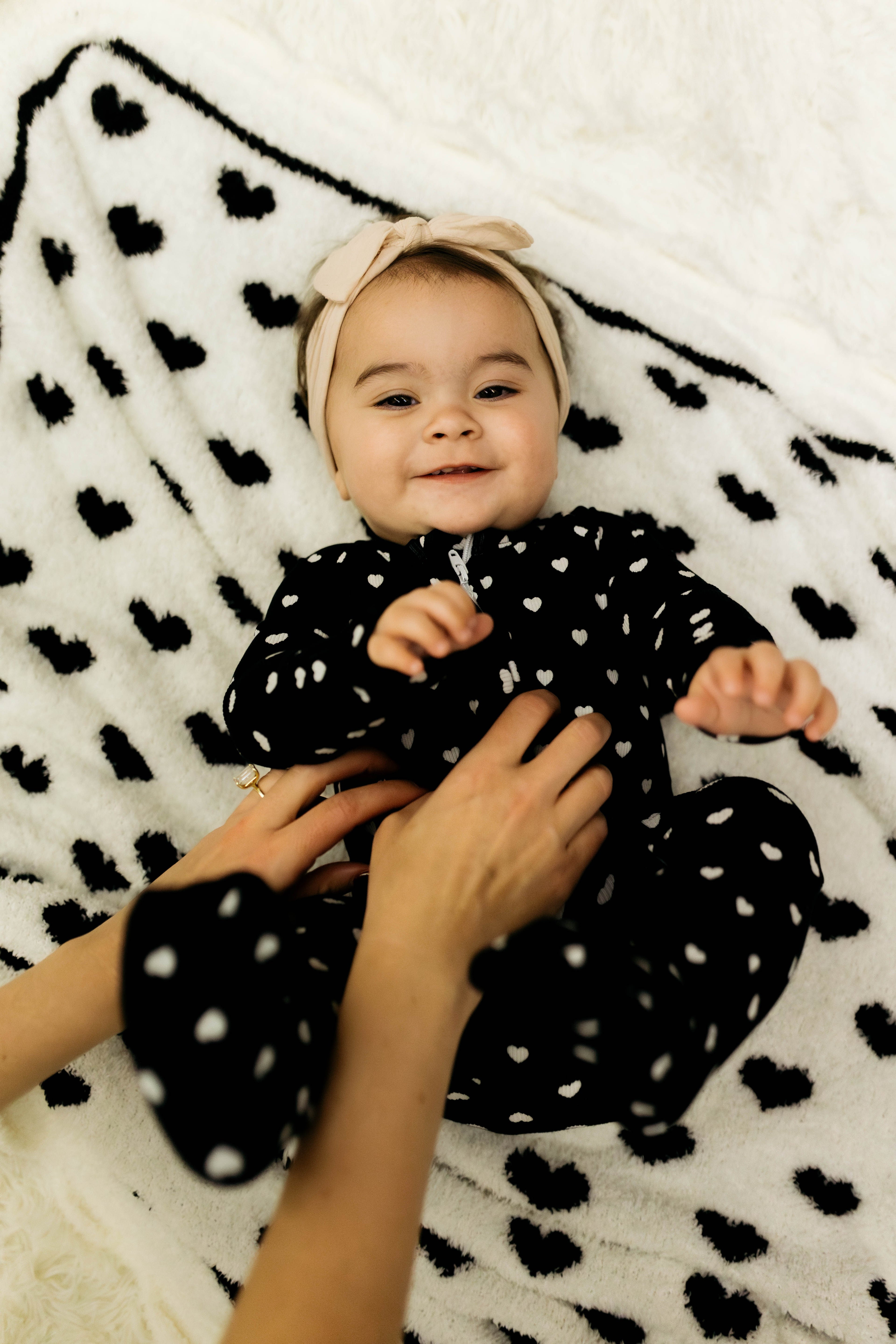 Baby in a black polka dot outfit lying on a white blanket with black heart patterns