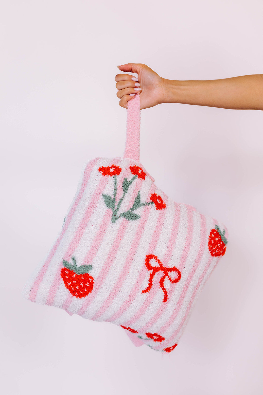 holding the strawberry backpack quillow by the wristlet