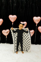 Child holding a heart-shaped blanket with pink heart balloons in the background