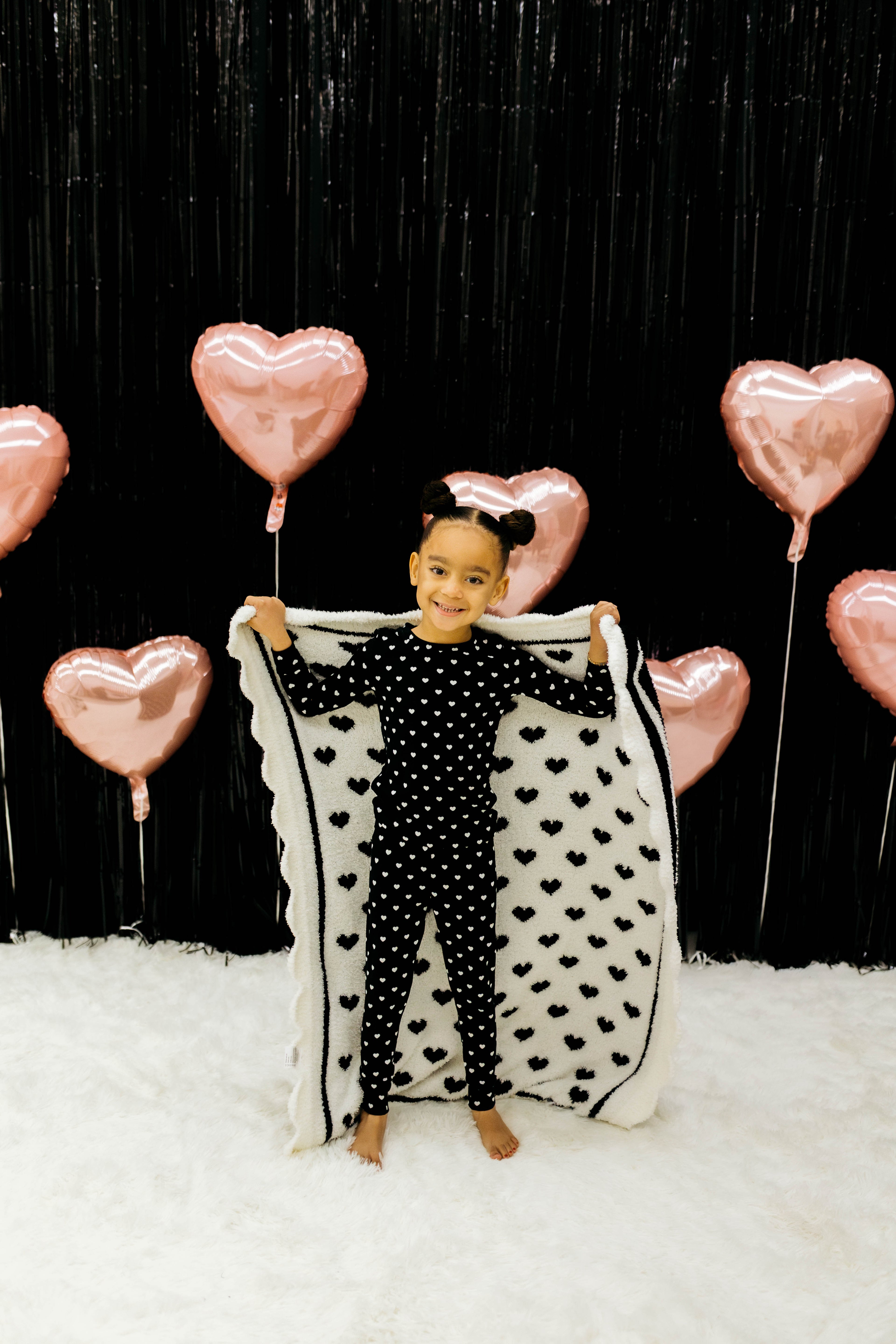 Child holding a heart-shaped blanket with pink heart balloons in the background