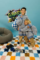 Two children in matching striped outfits standing on a colorful checkered floor with gaming equipment around.