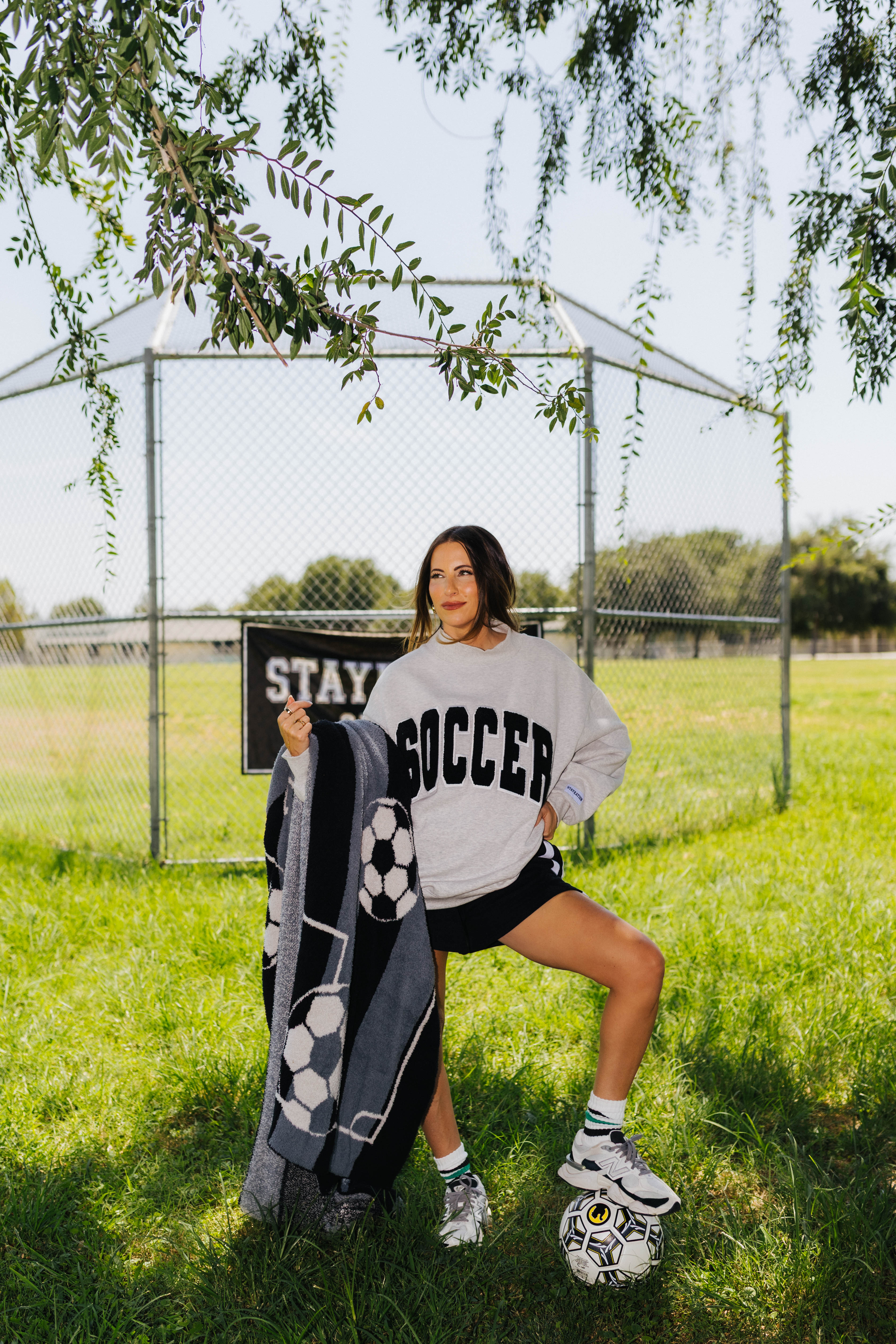 Woman standing in the field with a soccer ball below her foot holding the soccer ball blanket.