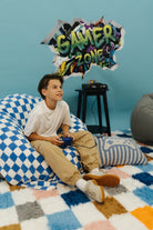 Young boy sitting on a bean bag chair in a room with 'Gamer Zone' decor.