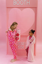 Two children in pink-themed outfits standing in front of a heart-shaped pink backdrop with 'BOOTH' and 'Kisses 50c' text.
