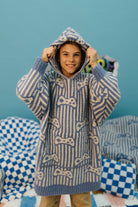 Child wearing a blue and white patterned sweater with a hood against a blue background.