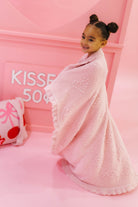 Child wrapped in a pink blanket against a pink background with 'Kiss' and '50 cents' text.