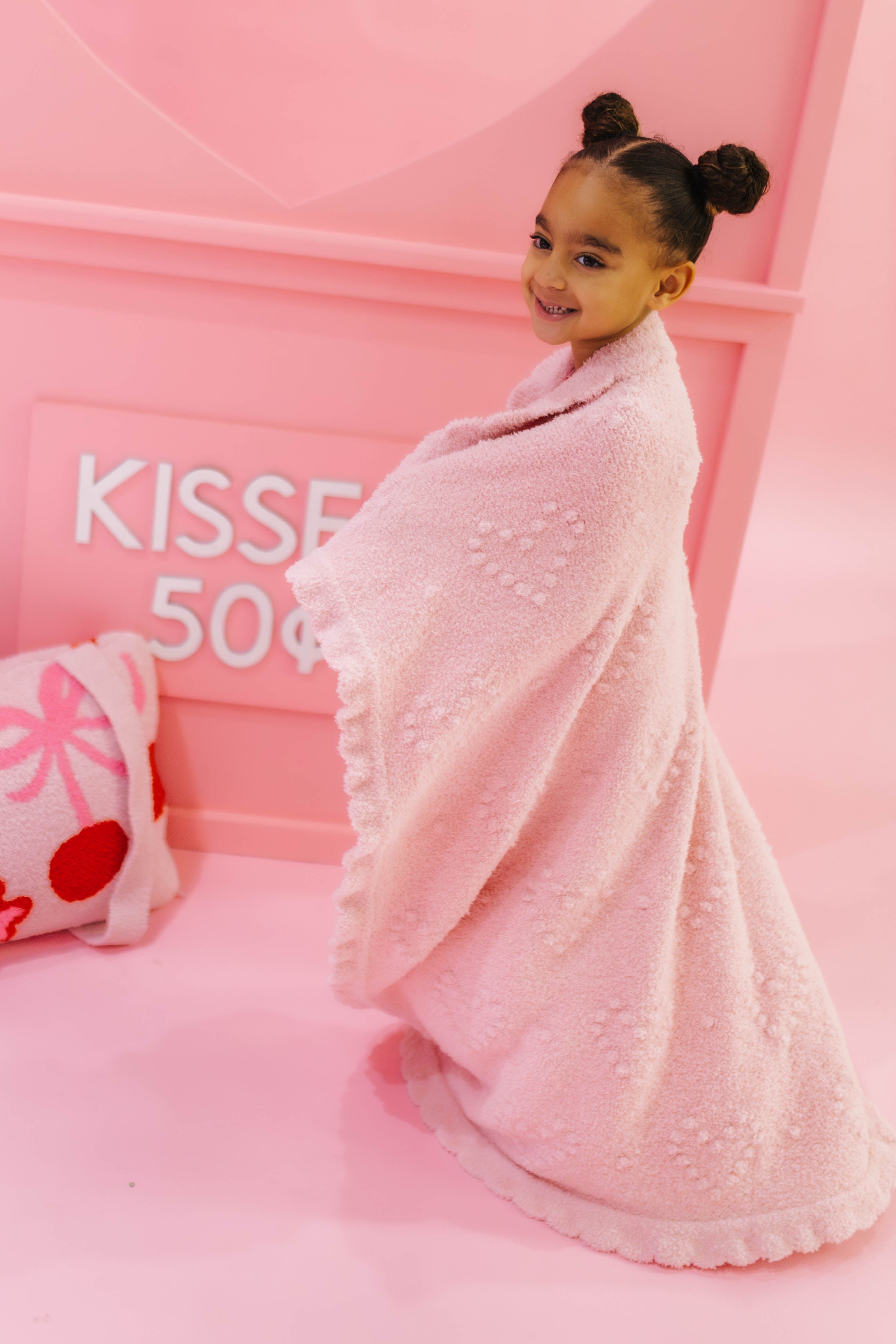 Child wrapped in a pink blanket against a pink background with 'Kiss' and '50 cents' text.