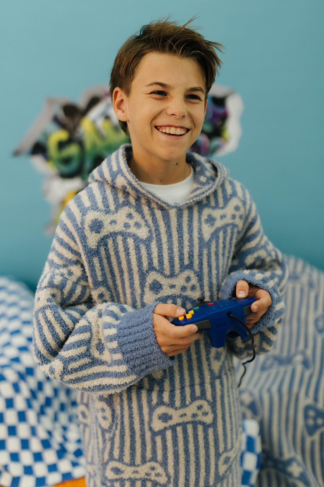 Young boy wearing a blue and white patterned sweater holding a blue toy in front of a blue wall with colorful letters.