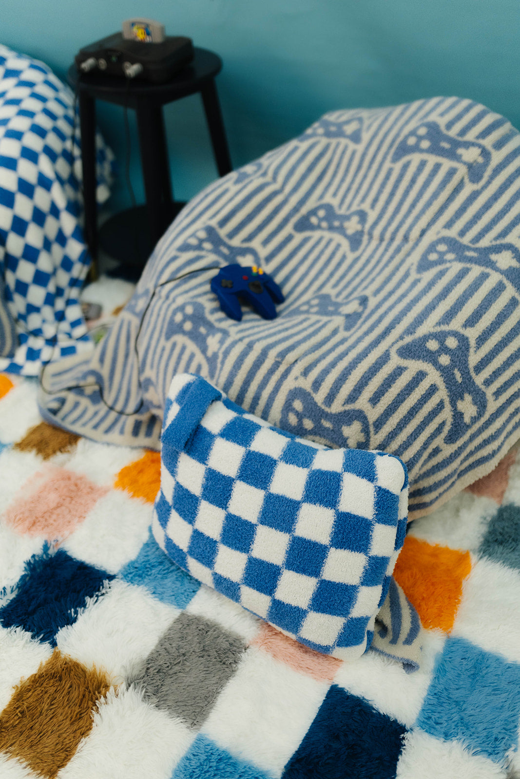 Blue and white checkered pillow on a colorful blanket with a blue wall background