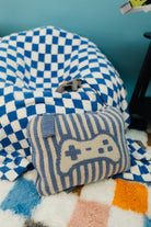 Blue and white checkered bean bag chair with a striped pillow featuring a game controller design on a colorful rug.