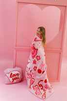 Person wrapped in a heart-patterned blanket with a pink heart-shaped door in the background
