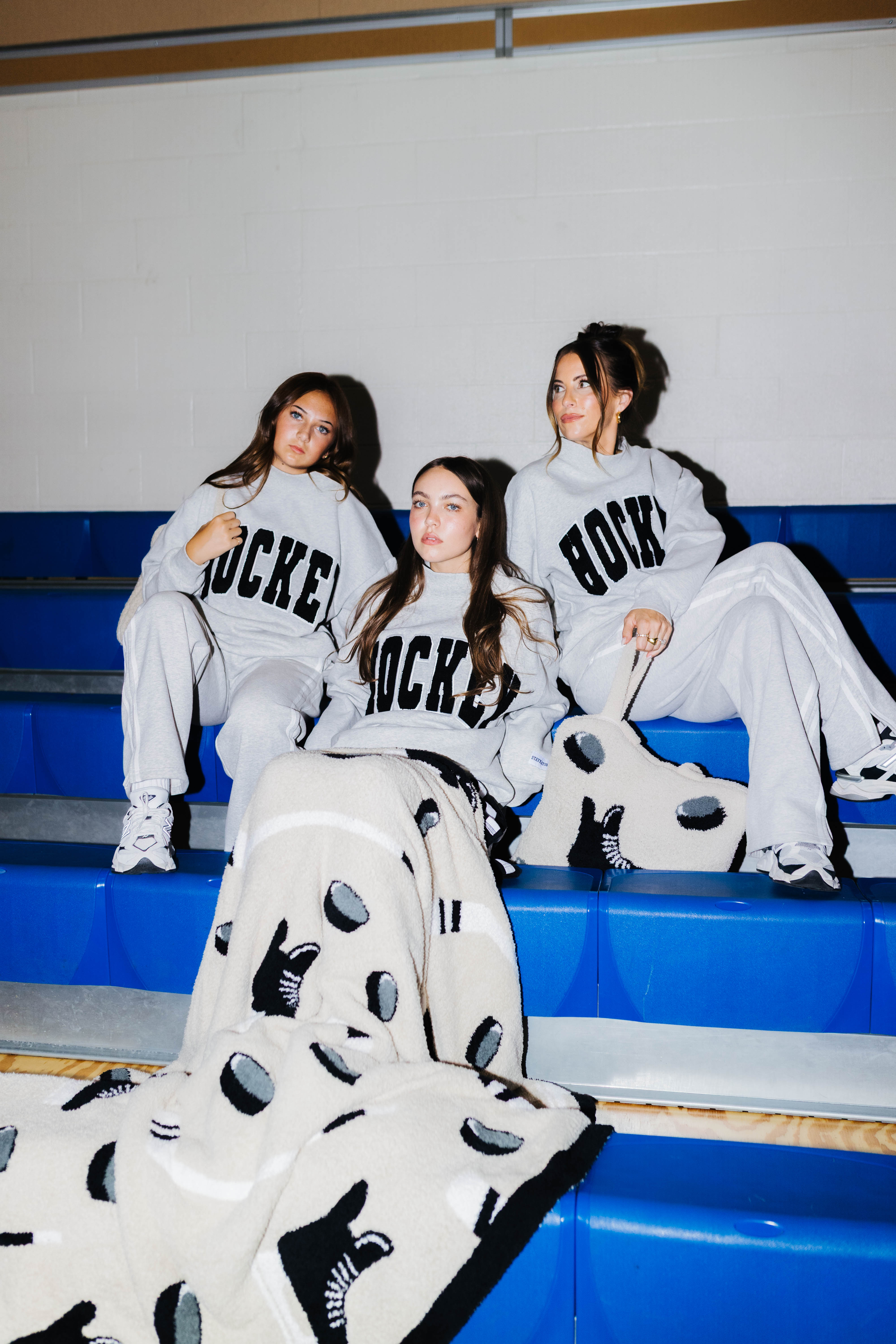 Girls on the bleachers waring matching outfits and the hockey blanket draped over the middle girl