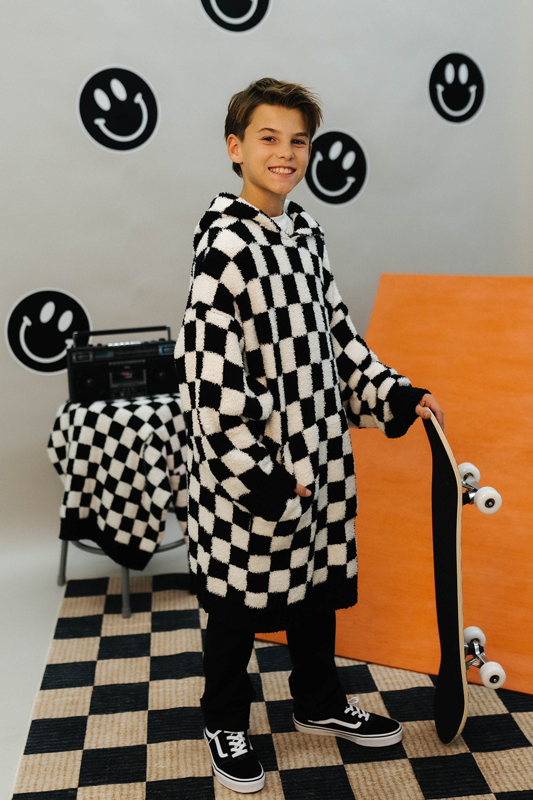 Person wearing a long black and white checkered wearable standing in a room with a checkered floor and smiley face decorations on the wall.