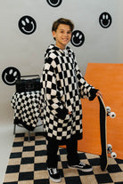 Person wearing a long black and white checkered wearable standing in a room with a checkered floor and smiley face decorations on the wall.