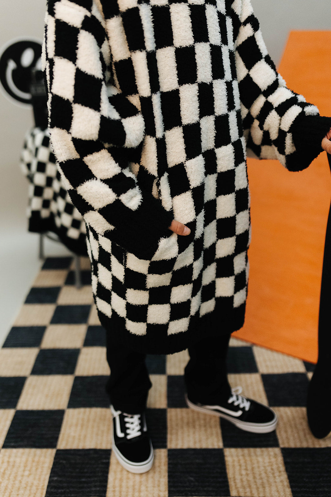 Person wearing a black and white checkered wearable with sneakers on a checkered floor.