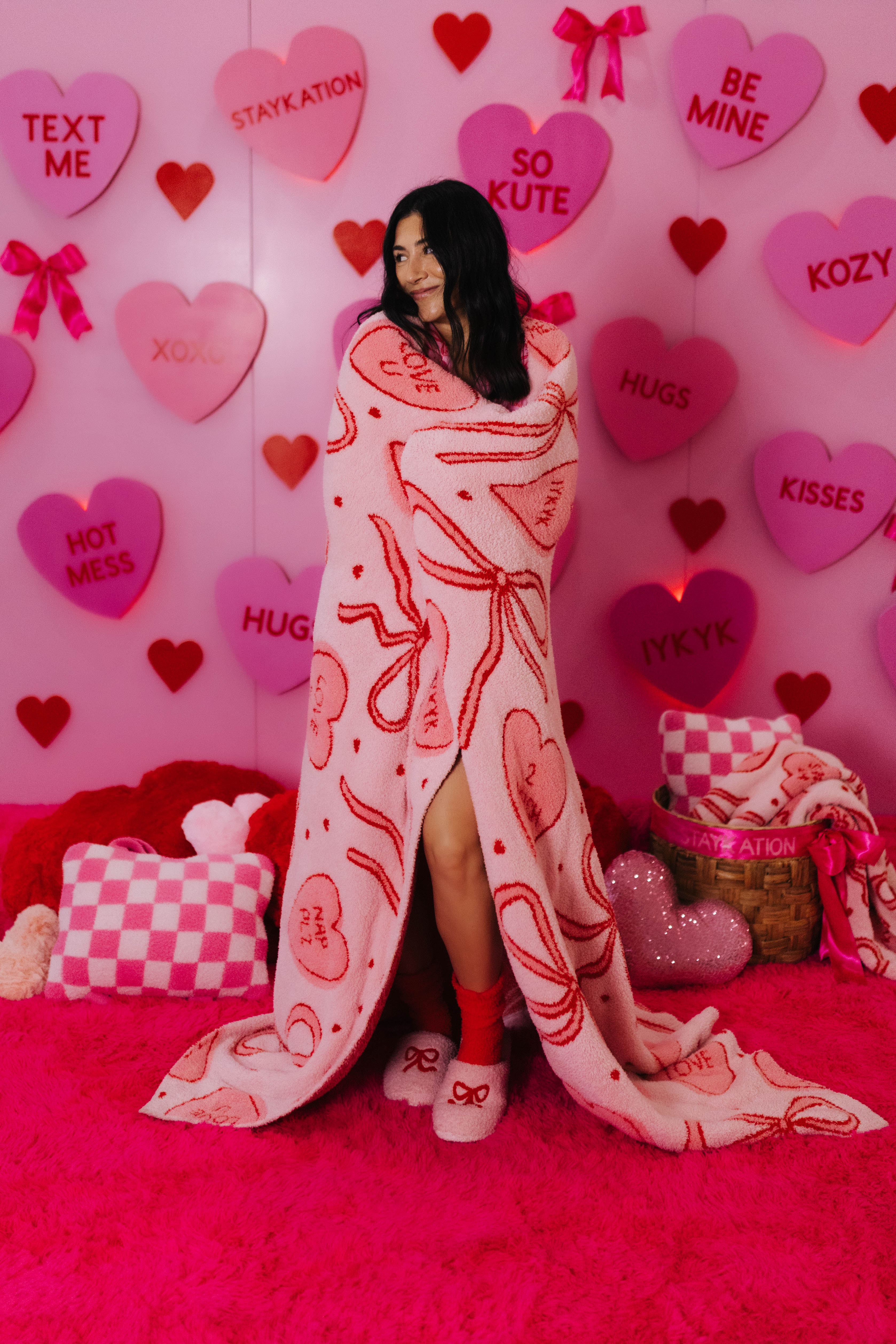 Person wrapped in a heart-themed blanket with a pink background featuring Valentine's Day decorations.