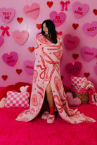 Person wrapped in a heart-themed blanket with a pink background featuring Valentine's Day decorations.